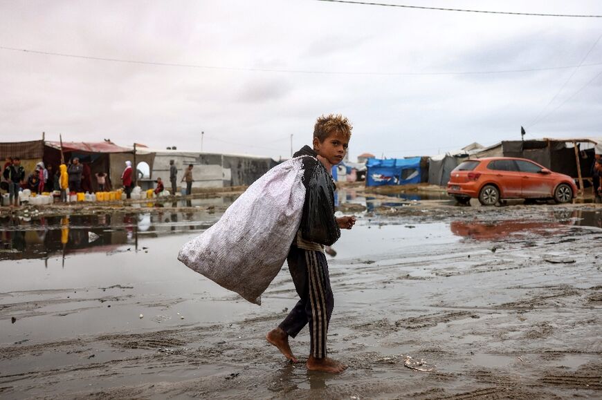 A displaced Palestinian child carrying a bag walks barefoot in a displacement camp in the central Gaza Strip 