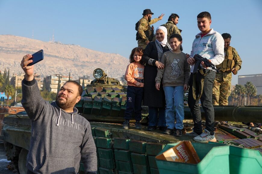 A man takes a selfie with his family standing atop a tank as they celebrate in Damascus on Monday