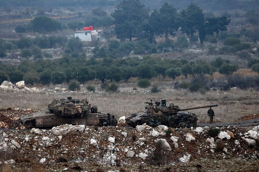 An Israeli army Merkava tank (L) is deployed near Israeli soldiers inspecting a Syrian army tank that they captured, in the UN-monitored buffer zone that they have entered on the Golan Heights, near Majdal Shams 