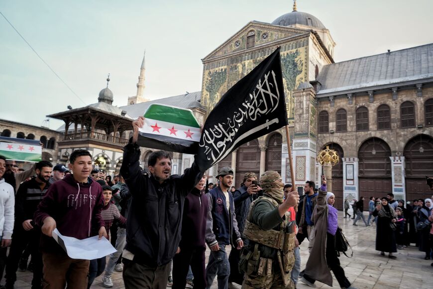 Syrians walk through the courtyard of the Umayyad Mosque in Damascus holding the new flag, at the front a rebel fighter holds the flag of Hayat Tahrir al-Sham on December 10, 2024. Photo credit: Morhaf Kiwan.