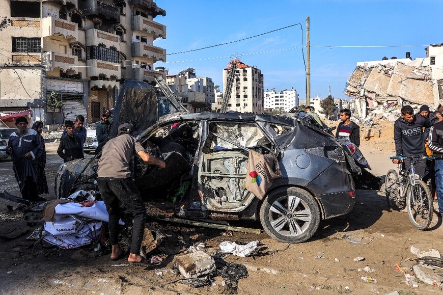 People inspect the remains of a car that was hit in central Gaza City