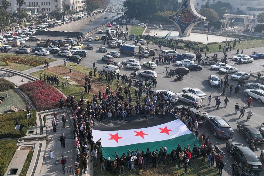 People celebrate with a large Syrian opposition flag at Umayyad Square in Damascus