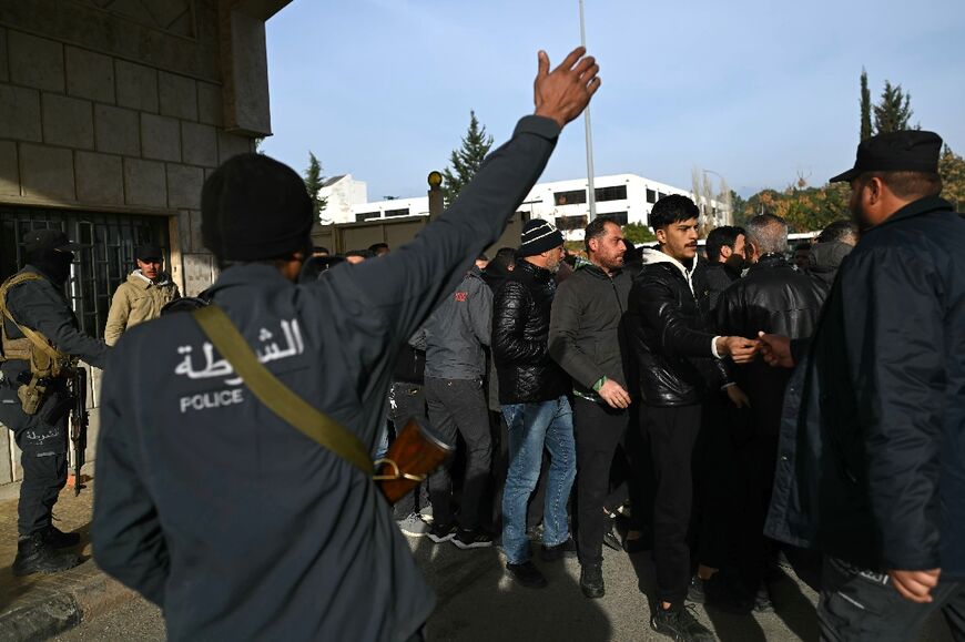 A member of Syria's new authorities shouts instructions at a crowd waiting to register or hand over their weapons, in the port city of Latakia