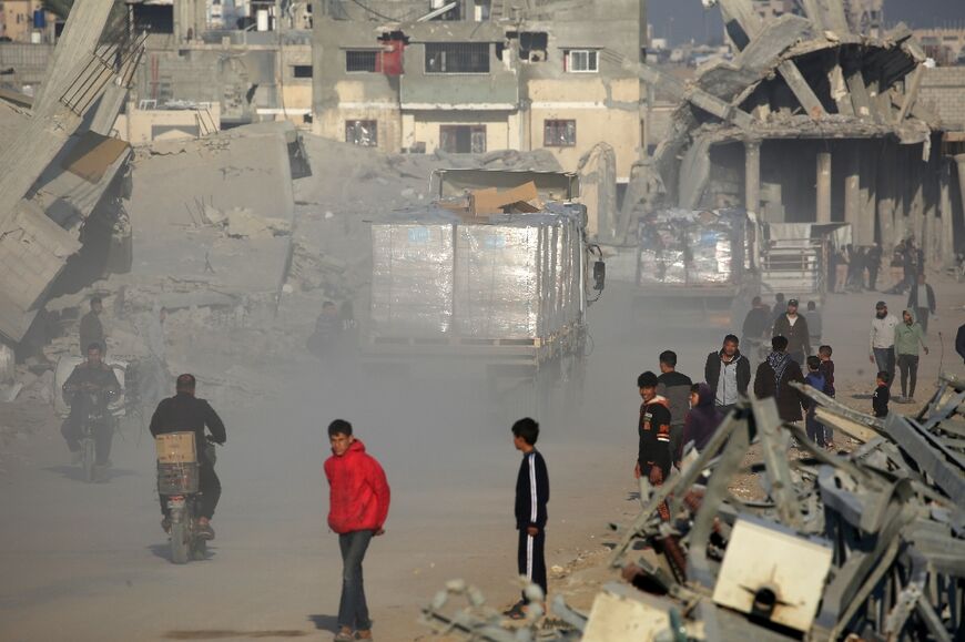 People watch as trucks loaded with humanitarian aid drive through a devastated street in Khan Yunis, southern Gaza