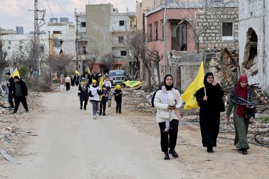 Residents of the southern Lebanese village of Khiam wave Hezbollah flags among the rubble of destroyed buildings