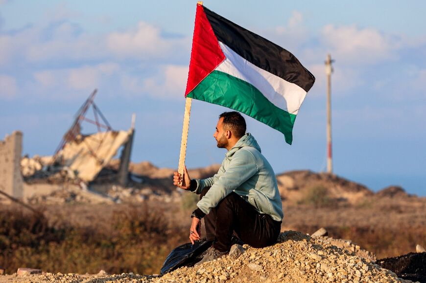 A man holds a Palestinian flag as he watches displaced Gazans cross the Netzarim corridor on Monday