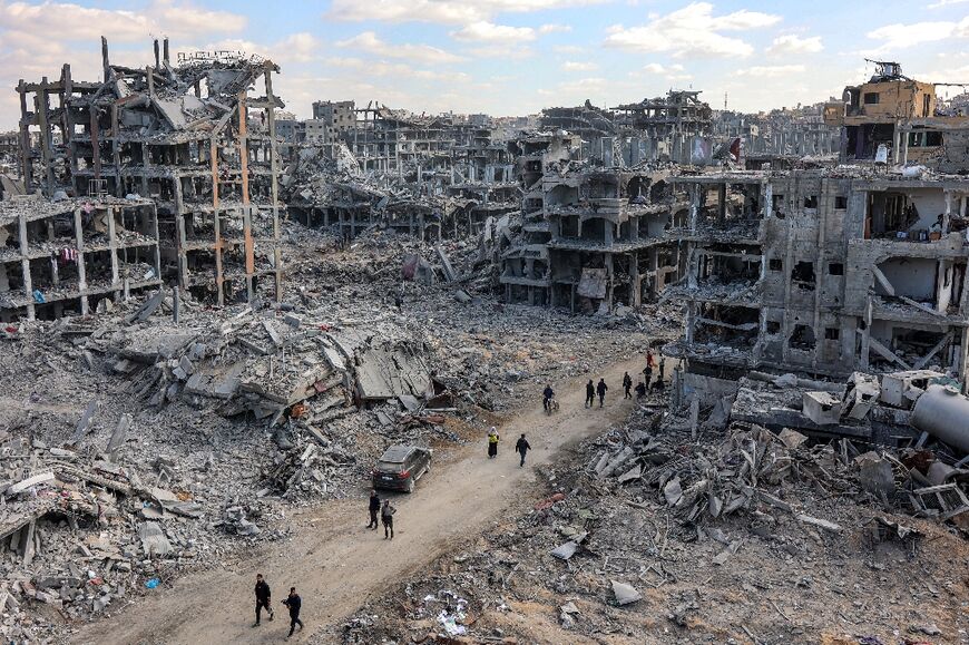 People walk past the rubble of damaged and collapsed buildings in Beit Lahia in the northern Gaza Strip