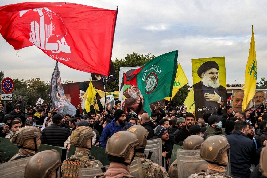 Protesters wave flags of the Lebanese Shiite movements Hezbollah and Amal with a portrait of slain Hezbollah leader Hassan Nasrallah near Lebanese soldiers during a rally blocking the road to Beirut International Airport