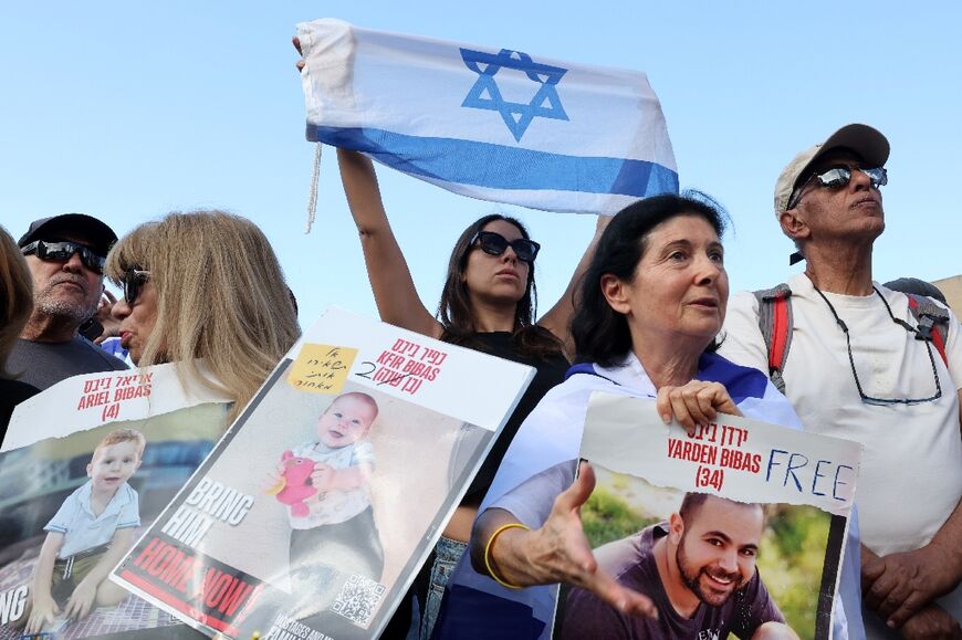 Onlookers with pictures of released hostage Yarden Bibas, as well as of his two children Kfir and Ariel