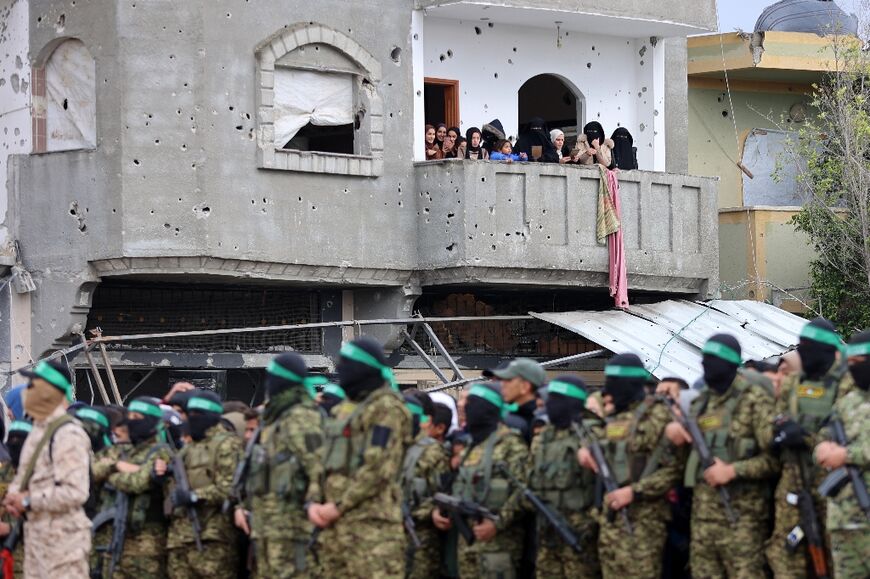 People watch from a battle-scarred buildings as Hamas fighters gather at the site of the handover of two Israeli hostages in Rafah, southern Gaza