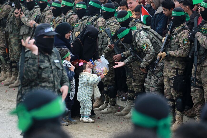 A Palestinian child offers candy to Hamas fighters in Nuseirat, central Gaza, ahead of their release of three Israeli hostages