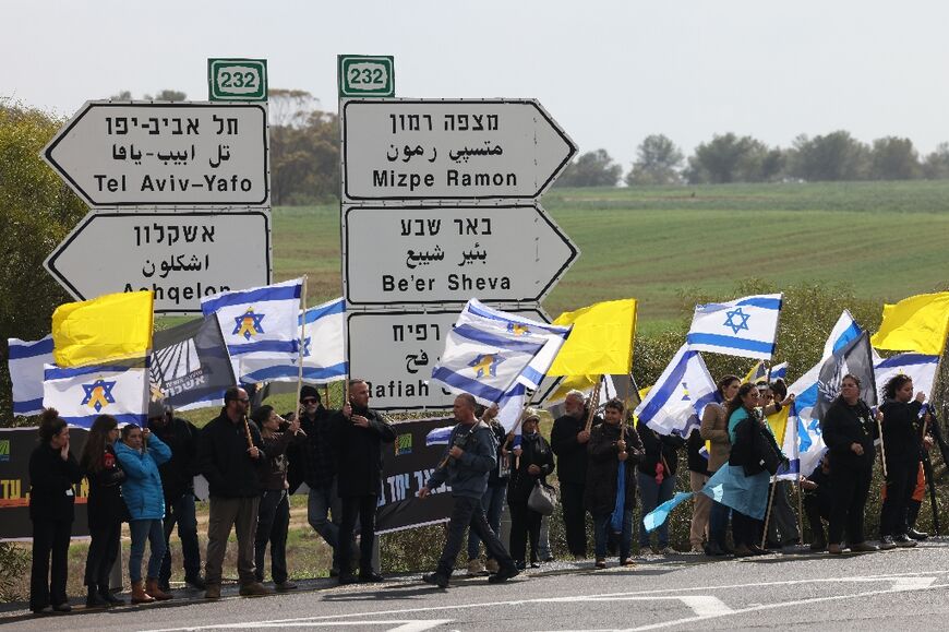 Israelis wave their national flag and yellow banners for hostages held in Gaza as they await the arrival near Kissufim, southern Israel, of hostages' bodies released by militants