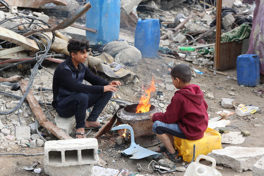 Palestinians warm themselves by a fire amid the rubble of destroyed buildings at Saftawi street in Jabalia, in the northern Gaza Strip, on February 5, 2025 during a ceasefire deal in the war between Israel and Hamas. Palestinian militant group Hamas lashed out on February 5, at President Donald Trump's shock proposal for the United States to take over the Gaza Strip and resettle its people in other countries, seemingly whether they want to leave or not. (Photo by Omar AL-QATTAA / AFP) (Photo by OMAR AL-QATT