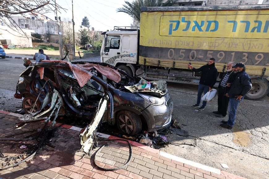 Men stare at a charred car that was hit by an Israeli strike in the occupied West Bank city of Qabatiya