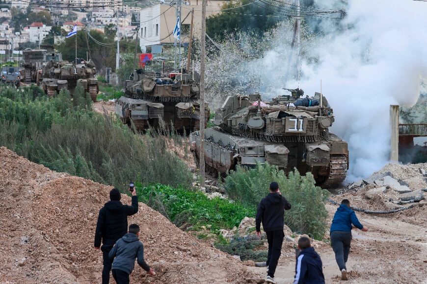 Palestinian youths throw stones and film Israeli tanks and bulldozers entering the Jenin camp for Palestinian refugees in the occupied West Bank