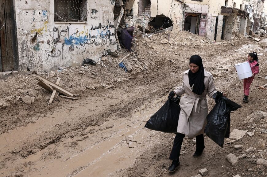 On March 3, 2025 a Palestinian woman carries her belongings on a bulldozed road next to damaged buildings in Jenin refugee camp after an Israeli military operation 