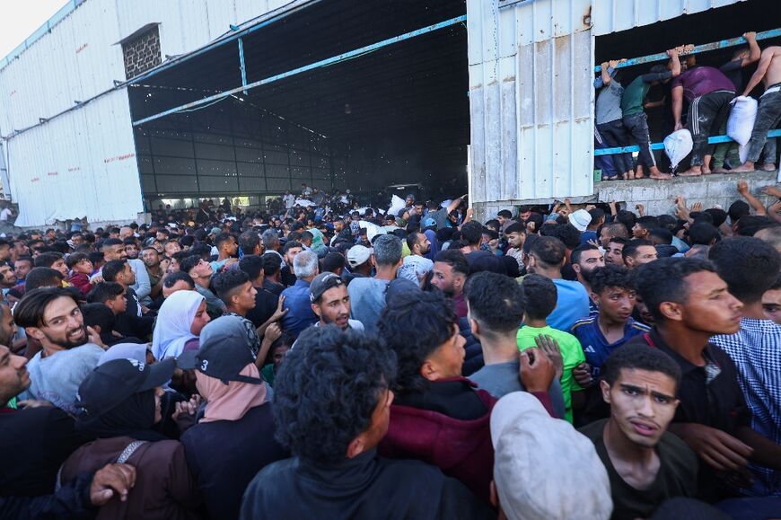 Displaced Palestinians ferry bags of food aid as they storm a World Food Programme warehouse in Deir el-Balah in the central Gaza Strip on May 28, 2025