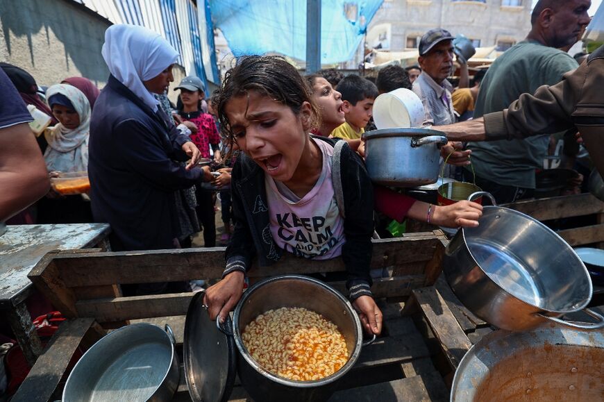 A girl reacts after receiving a cooked meal as others wait at a distribution point in Nuseirat, central Gaza Strip, on June 2