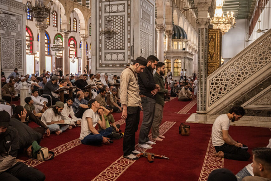 A man prays with a gun at his feet in Umayyad Mosque in central Damascus before midday Friday prayers during Eid on June 6, 2025 in Damascus, Syria. Eid al-Adha is the second of Islam's two main festivals. (Photo by Ed Ram/Getty Images)