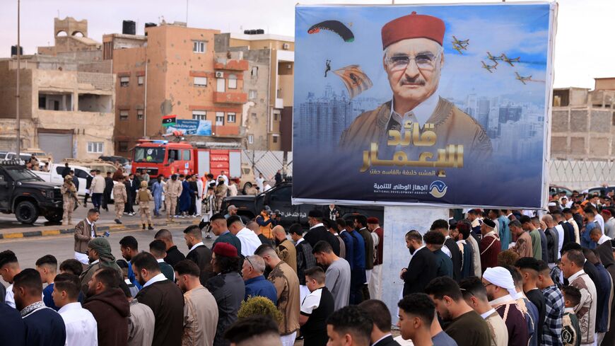 Security forces stand guard as Libyans perform the morning prayer of Eid al-Fitr, which marks the end of the Muslim holy fasting month of Ramadan, outdoors with a portrait of the military strongman of eastern Libya, Khalifa Haftar, in the backgound in the heart of the Mediterranean port city of Benghazi on March 31, 2025. 