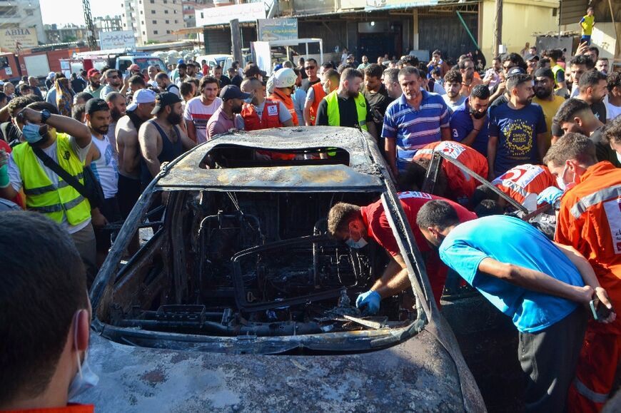 Onlookers gather around a burnt out car targeted in an Israeli strike near Lebanon's main northern city of Tripoli.