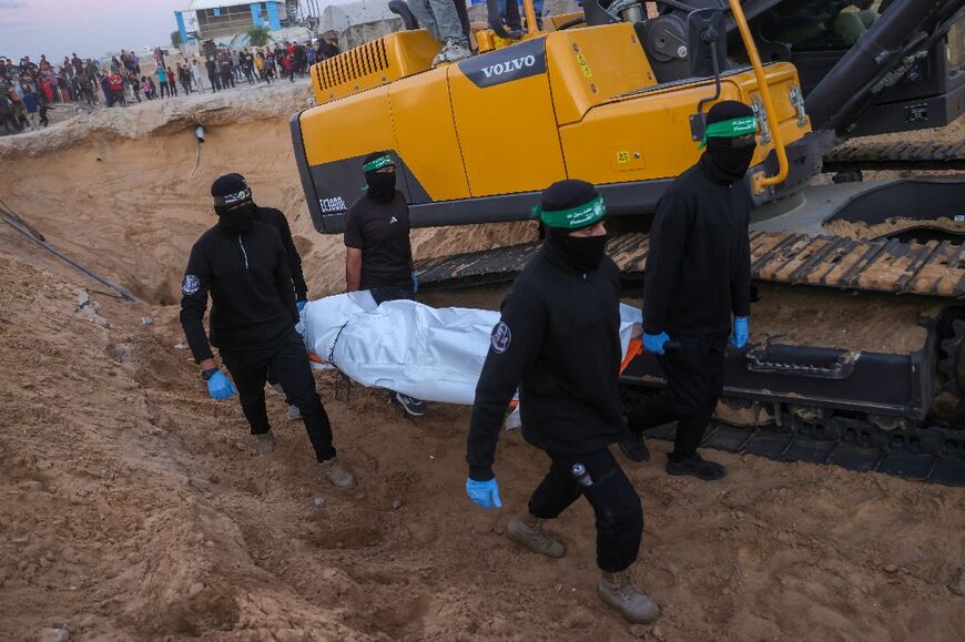 People look on as Hamas militants carry a body retrieved from a tunnel in an area north of Khan Yunis on Tuesday