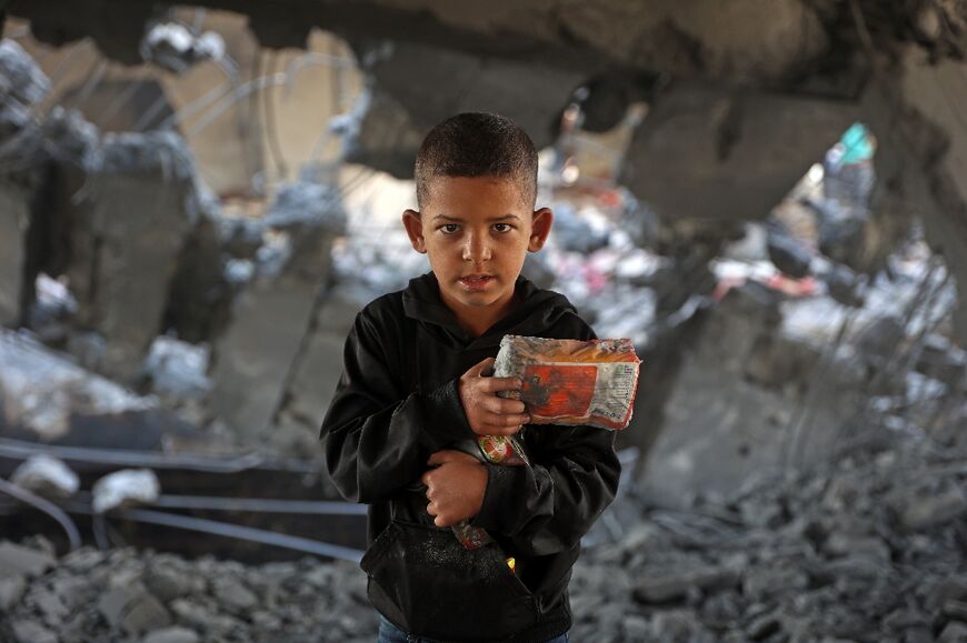 A Palestinian boy holds his belongings amid the debris of a damaged building in Zeitoun