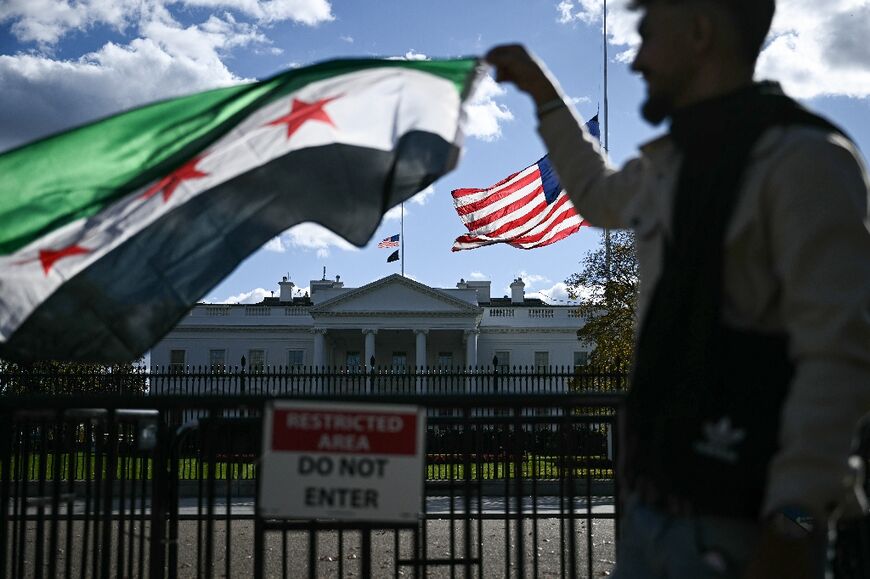 A man holds a Syrian flag across the street from the White House after Syrian President Ahmed al-Sharaa's meeting with US President Donald Trump 