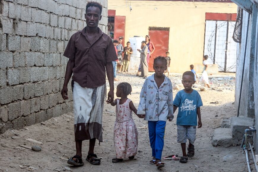 Somali refugee Abdallah Omar walks with his children along an alleyway in Aden on October 23, 2025