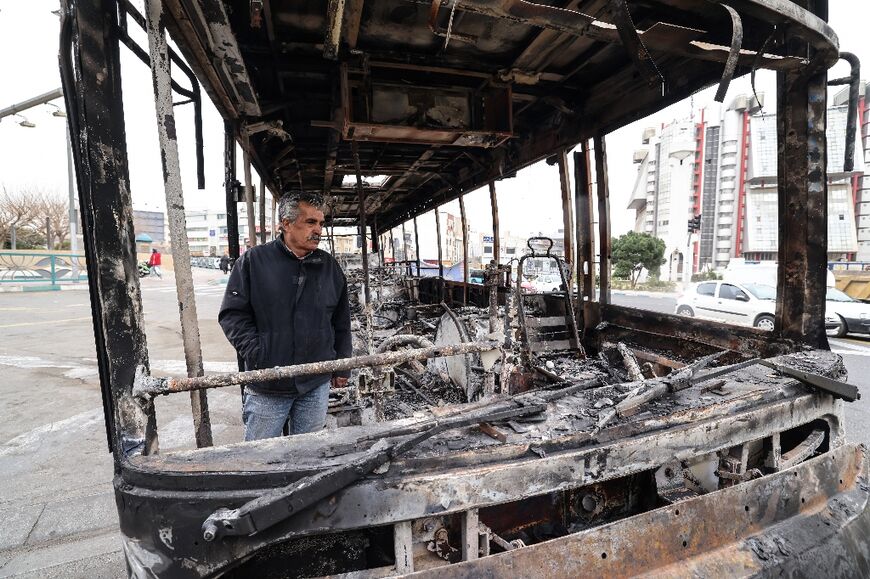 A man stands in the wreckage of a burned bus in Tehran's Sadeghieh Square on January 15, 2026