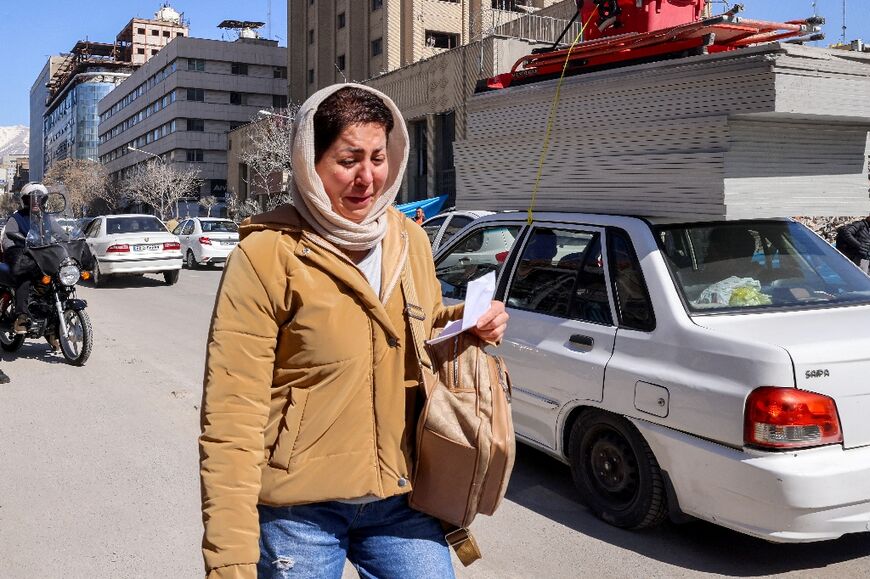 A woman reacts while walking past collapsed and damaged buildings near Ferdowsi square in Tehran 