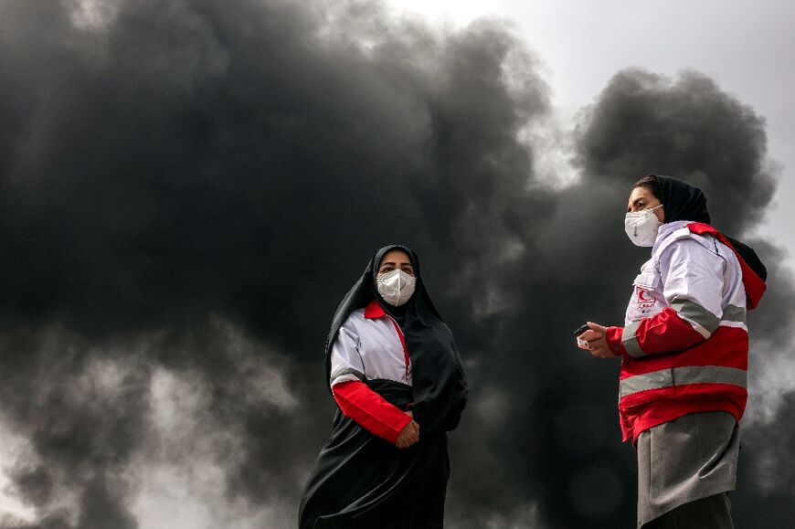Members of Iran's Red Crescent society stand near smoke caused by an overnight on an oil facility in northwestern Tehran 
