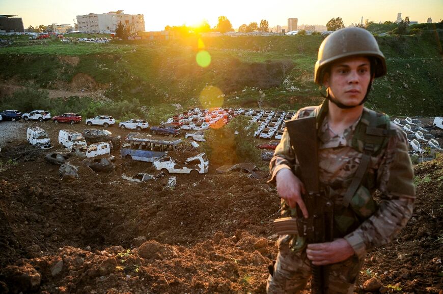 A Lebanese Army soldier stands guard in front of destroyed vehicles at a parking lot in Dekwaneh, on the eastern outskirts of Beirut