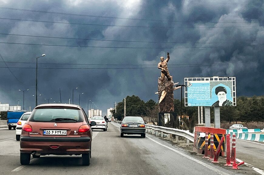 Plumes of black smoke mix with rain clouds in the skies of Tehran