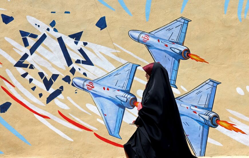 A woman walks past an anti-US and anti-Israel mural in Tehran