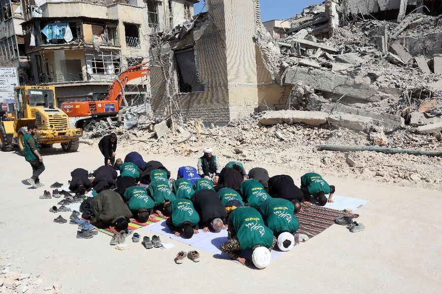 Iranian clerics and volunteers from the Basij paramilitary group pray next to the rubble of a destroyed police station in Tehran on March 4