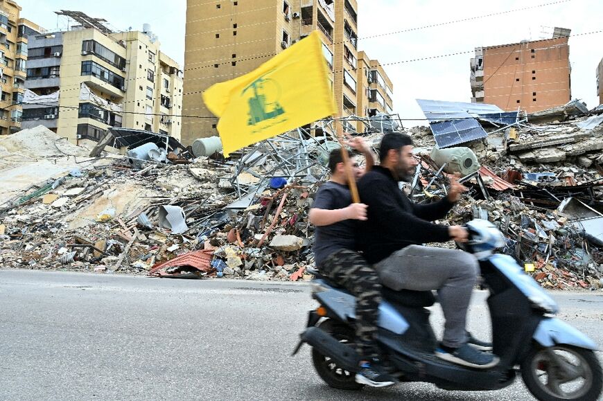 Residents of southern Beirut fly the Hezbollah flag as they ride past destroyed buildings