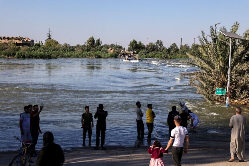 People stand at the site of a collapsed bridge while they wait for assistance to cross the river