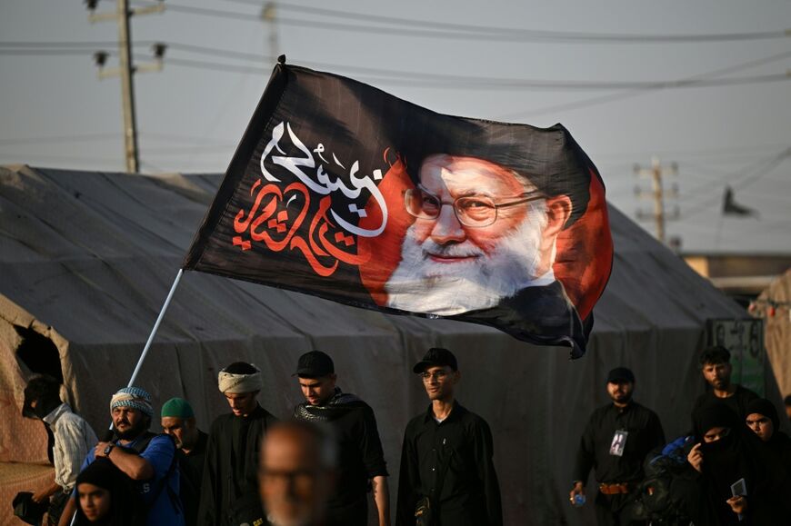 Shiite Muslim pilgrims hold a flag bearing the portrait of Iran's slain supreme leader Ayatollah Ali Khamenei